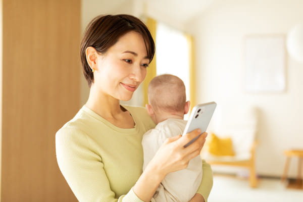 赤ちゃんを抱っこしながらスマートフォンを触る女性